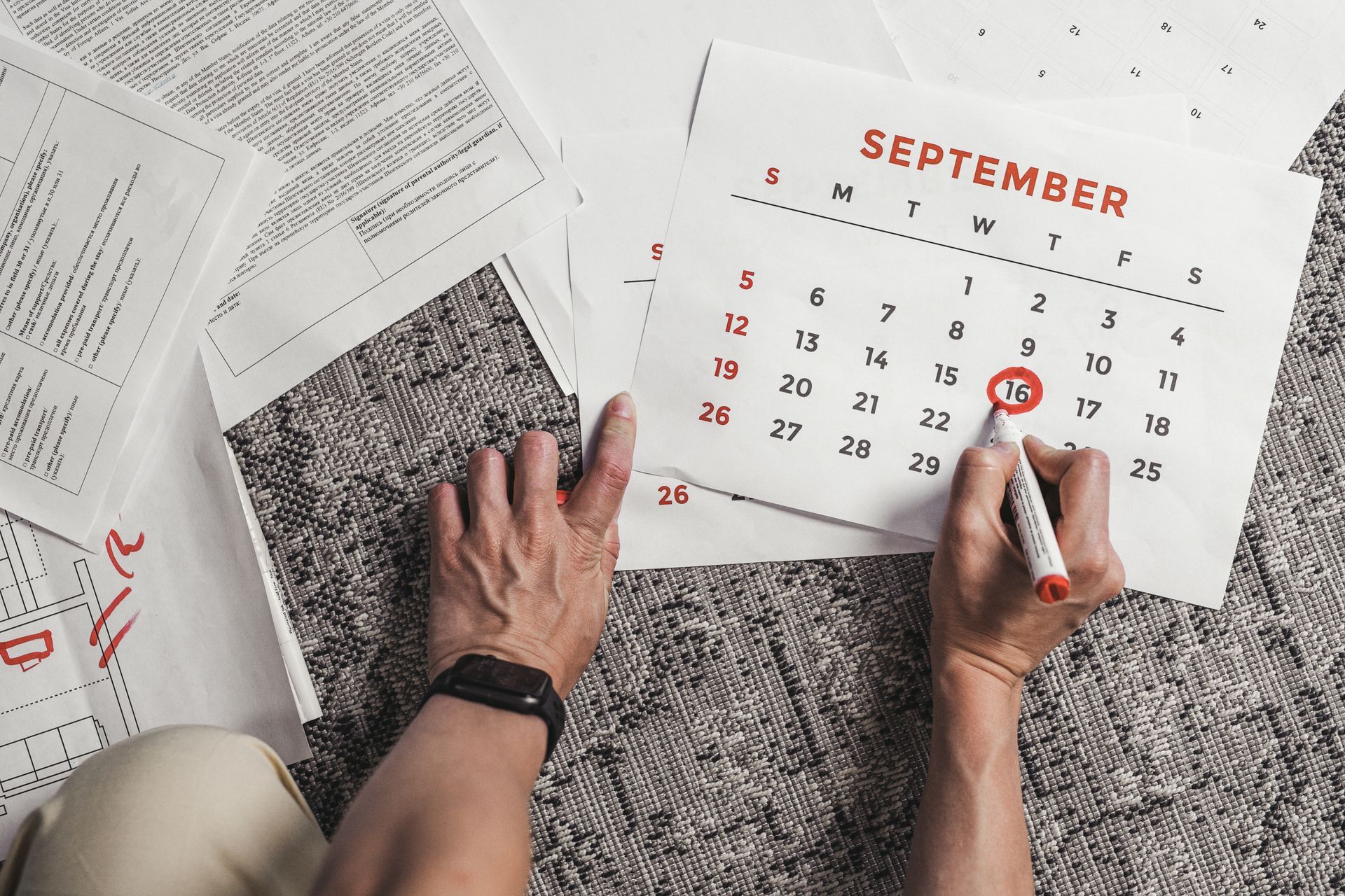 Mãos circulando a data da viagem no calendário, com os documentos da mudança espalhados ao redor